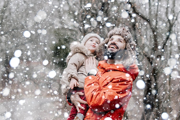 Joven elegante barbudo Padre e hijo en vacaciones de invierno cerca del árbol de Navidad Padre dando a su hijo un paseo en el parque Feliz familia alegre Papá arroja a una niña