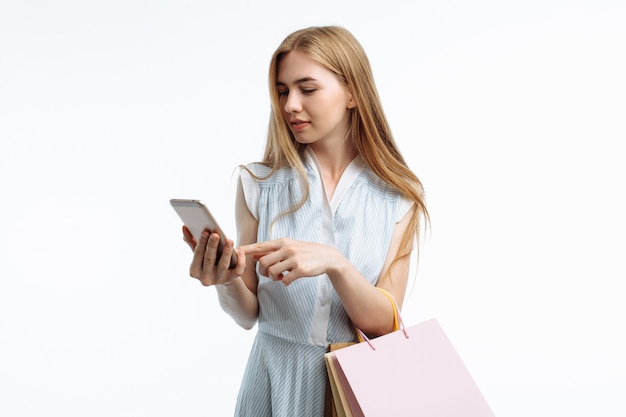 Joven elegante, con bolsas de regalo, posando en las manos del teléfono