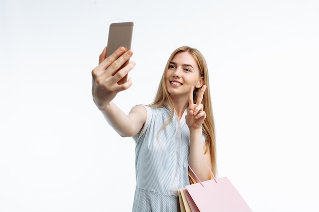 Foto joven elegante, con bolsas de regalo, posando y tomando una selfie en el teléfono con bolsas de compras