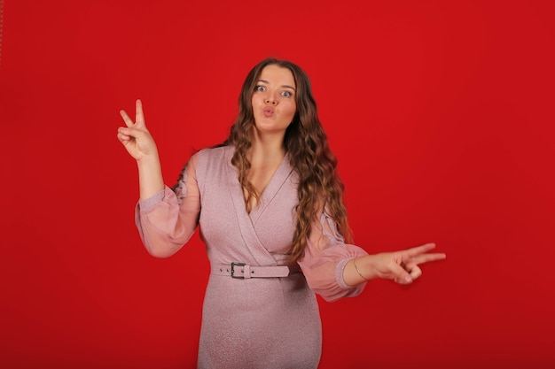 Una joven elegante con cabello largo con un vestido rosa sobre un fondo rojo muestra emoción.