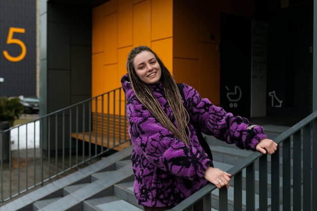 Una joven elegante con dreadlocks se encuentra contra el fondo de una casa naranja