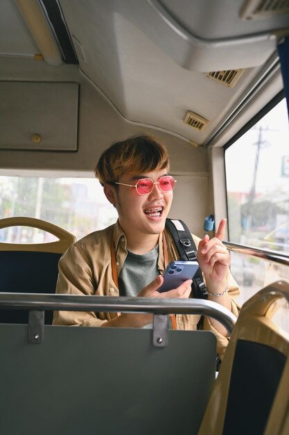 Un joven elegante enviando mensajes de texto en su teléfono inteligente viajando en autobús Concepto de transporte público