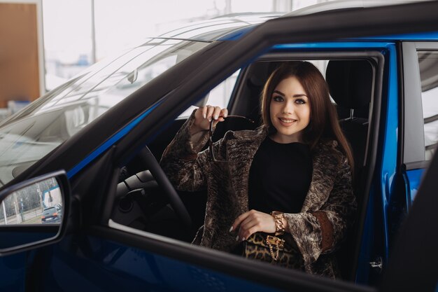 Una joven elegante está eligiendo un auto nuevo en una tienda de autos