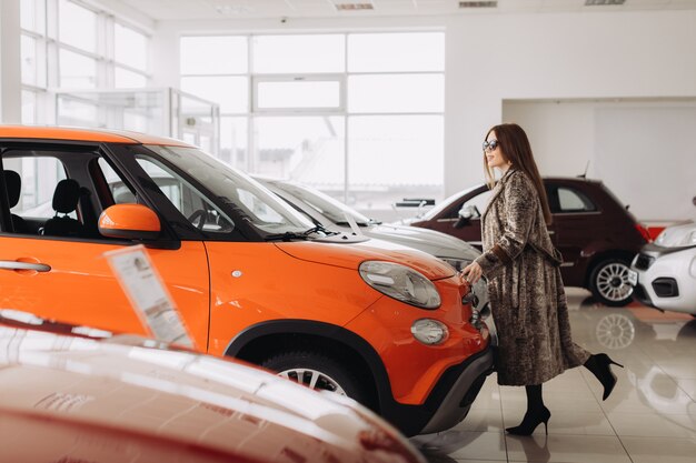 Una joven elegante está eligiendo un auto nuevo en una tienda de autos