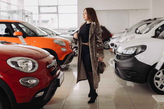 Una joven elegante está eligiendo un auto nuevo en una tienda de autos