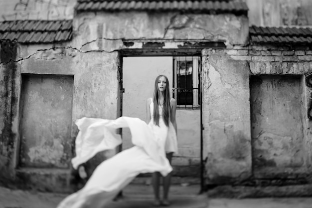 Joven elegante romántica en vestido blanco largo volando posando sobre edificios antiguos de piedra