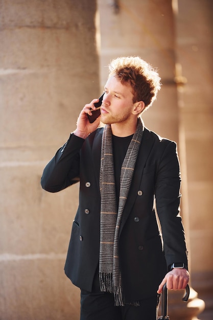 Un joven elegante con ropa elegante y formal de pie y hablando por teléfono al aire libre en la ciudad