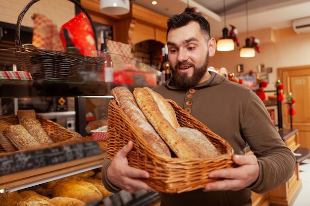 Joven eligiendo pan fresco de la canasta en la panadería