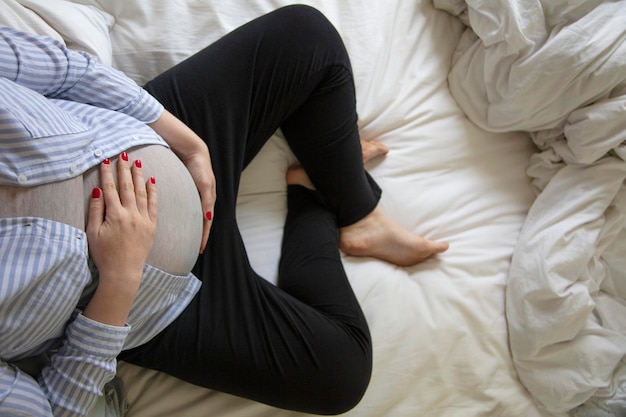 Una joven embarazada descansando en casa sentada en una cama futura madre