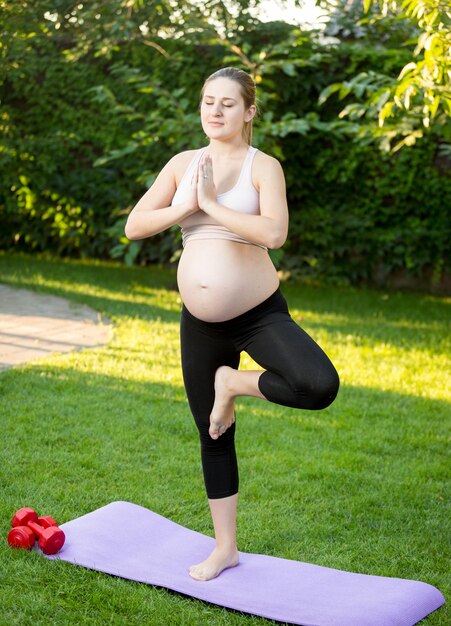 Joven embarazada haciendo ejercicio de yoga sobre el césped