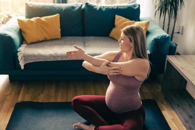 Joven embarazada haciendo yoga en casa por la mañana. Ella está haciendo ejercicios de estiramiento en su sala de estar.