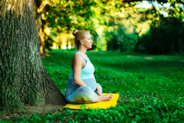 Joven embarazada haciendo yoga en el parque