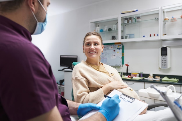 Joven embarazada con una hermosa sonrisa escucha al dentista en la clínica dental