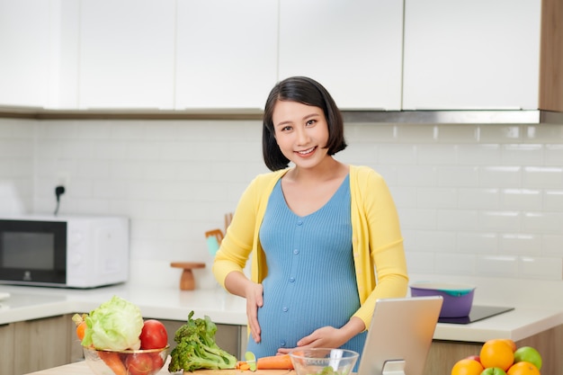 Joven embarazada preparando alimentos saludables con muchas verduras en la cocina de casa