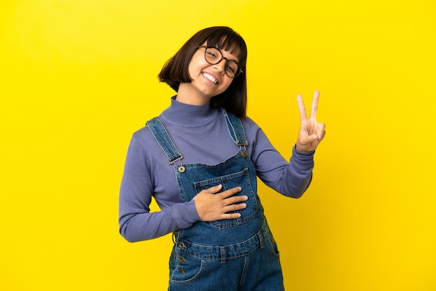 Joven embarazada sobre fondo amarillo aislado sonriendo y mostrando el signo de la victoria