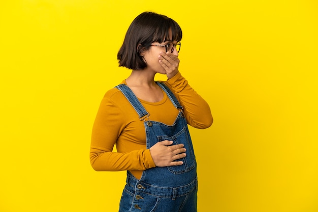 Foto joven embarazada sobre pared amarilla aislada que cubre la boca y mirando hacia el lado