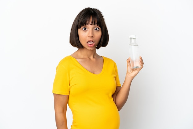 Joven embarazada sosteniendo una botella de agua aislada sobre fondo blanco con expresión facial sorpresa