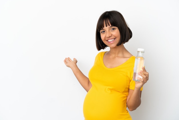 Joven embarazada sosteniendo una botella de agua aislado sobre fondo blanco extendiendo las manos hacia el lado para invitar a venir