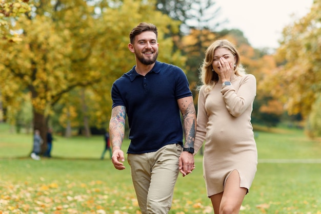 Joven embarazada y su apuesto esposo caminan en el parque de otoño