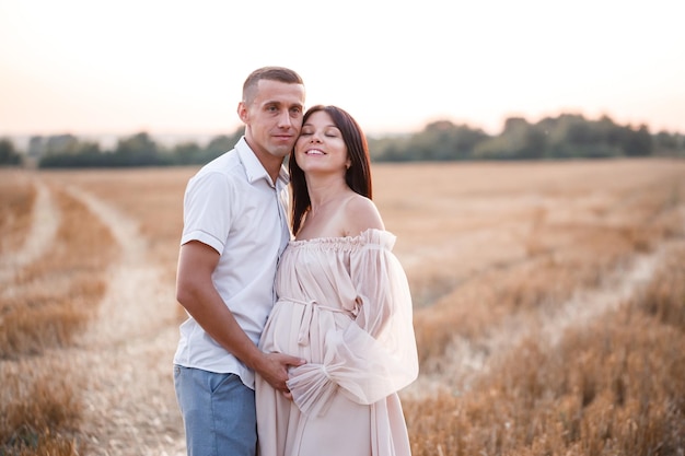 Una joven embarazada con su esposo, una hermosa pareja feliz abrazándose en un campo dorado en el campo Relaciones familiares Futuros padres