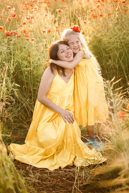 Una joven embarazada con su hija vestida de amarillo está parada en un campo de amapolas Relaciones familiares