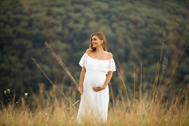 Joven embarazada en vestido blanco en el campo de verano