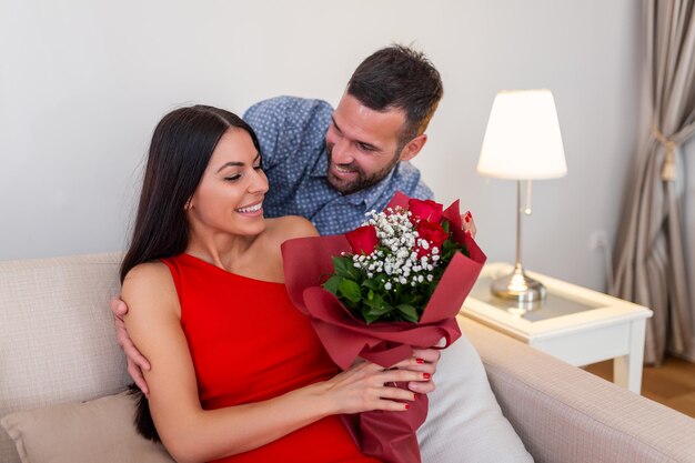 Una joven emocionada que recibe un ramo inesperado de rosas rojas de su esposo en casa, un novio generoso y cariñoso que hace una sorpresa romántica a una novia atractiva en la ocasión del día de San Valentín