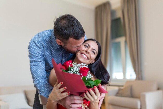 Una joven emocionada recibiendo un ramo inesperado de rosas rojas de su marido en casa el día de San Valentín