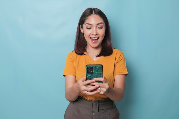 Una joven emocionada sonríe mientras sostiene su teléfono inteligente en la mano aislada de fondo azul