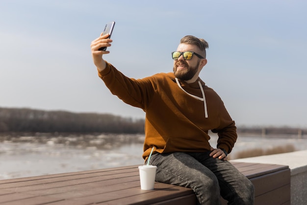 Un joven emocionado se está haciendo una selfie en un teléfono inteligente, es de la generación z o del milenio y lleva una moda informal