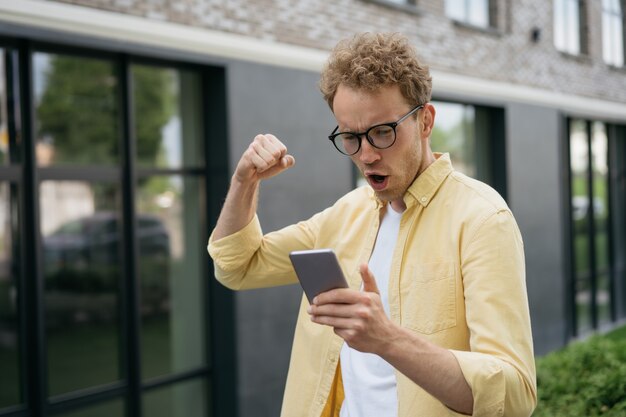 Joven emocional viendo televisión en línea usando la aplicación móvil para apuestas deportivas