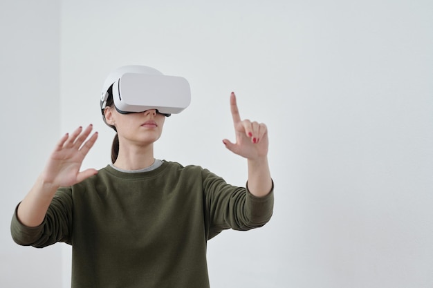 Joven empleada contemporánea apuntando a objetos en realidad virtual