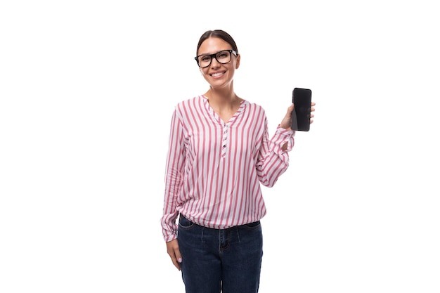 Foto una joven empleada de oficina vestida con una blusa blanca rosada y vaqueros muestra la pantalla de su teléfono inteligente con