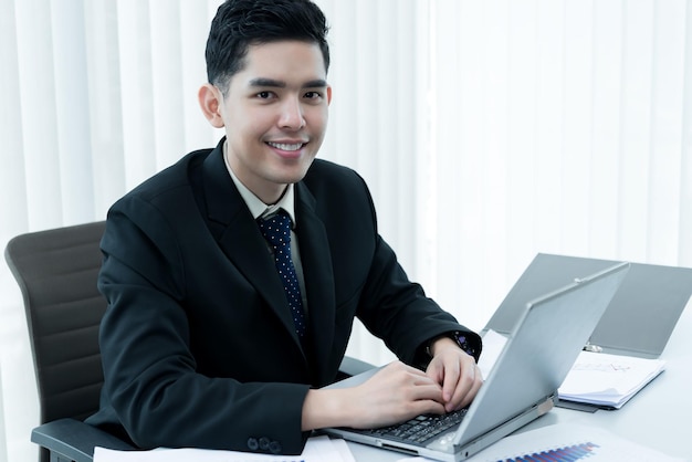 Joven empleado asiático que trabaja en una computadora portátil durante la jornada laboral en la oficinaEmpresario feliz con una sonrisa en la oficinagente tailandesa en la empresa