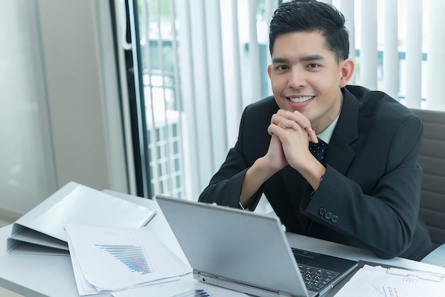 Joven empleado asiático que trabaja en una computadora portátil durante la jornada laboral en la oficinaEmpresario feliz con una sonrisa en la oficinagente tailandesa en la empresa