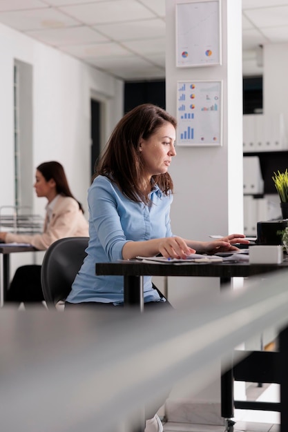 Joven empleado serio de la empresa que trabaja en un espacio de coworking, trabajador corporativo sentado en el escritorio del lugar de trabajo, vista lateral. Atractiva mujer seria usando laptop, gerente en oficina moderna