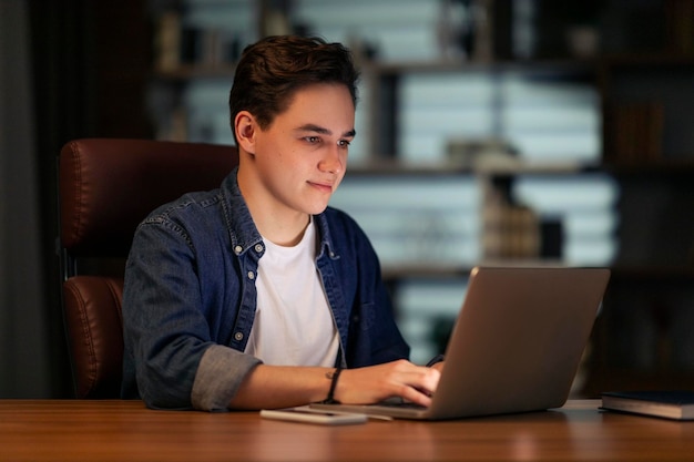 Joven emprendedor que trabaja en una oficina oscura usando una computadora portátil