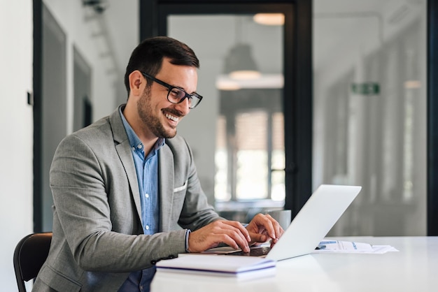 Foto joven emprendedor sonriente escribiendo en una laptop mientras trabaja en la oficina