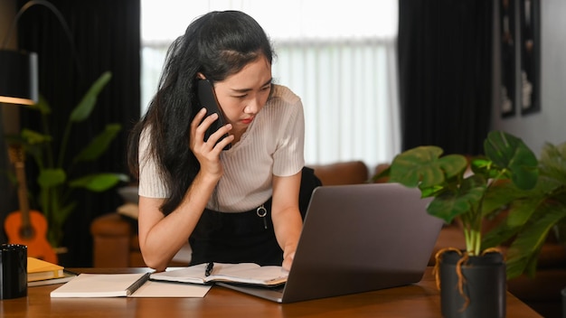 Joven emprendedora de negocios que tiene una conversación telefónica con su socio comercial que trabaja en la oficina de su casa