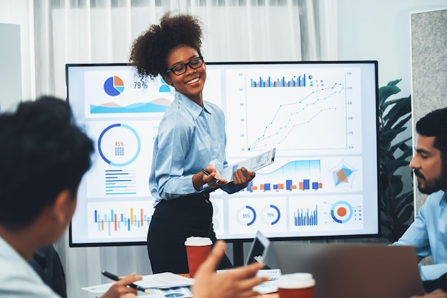 Joven empresaria africana que presenta un tablero de análisis de datos en la pantalla de TV en una reunión moderna Presentación de negocios con un grupo de empresarios en la sala de conferencias Concord