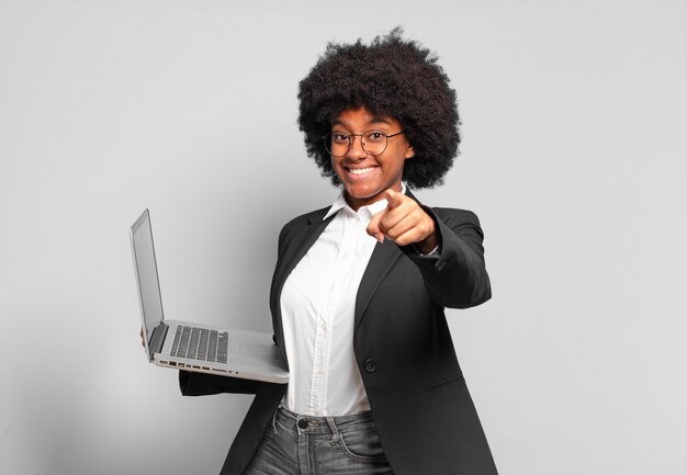 Joven empresaria afro apuntando con una sonrisa satisfecha, confiada y amistosa, eligiéndote. concepto de negocio