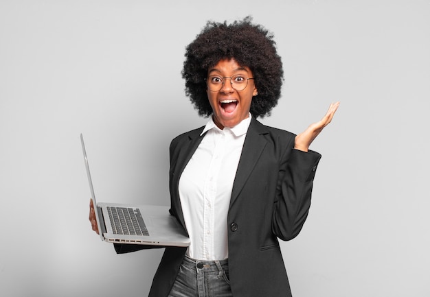 Joven empresaria afro que se siente feliz, emocionada, sorprendida o consternada, sonriendo y asombrada por algo increíble. concepto de negocio