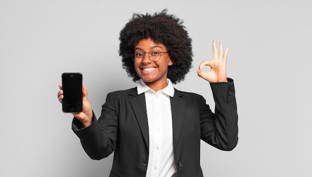 Joven empresaria afro que se siente feliz, relajada y satisfecha, mostrando aprobación con gesto bien, sonriendo. concepto de negocio