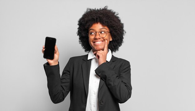 Joven empresaria afro sonriendo felizmente y soñando despierto o dudando, mirando hacia un lado. concepto de negocio