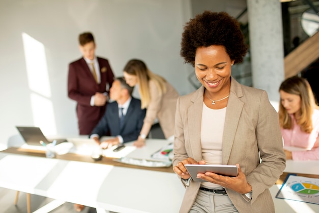 Joven empresaria afroamericana de pie y con tableta digital en la oficina moderna