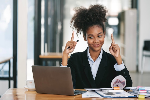 Una joven empresaria afroamericana sonriente que trabaja en línea en su escritorio usando una laptop para videollamadas