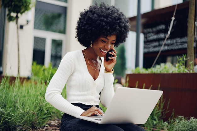 Joven empresaria afroamericana trabajando con una laptop sentada en el banco de la ciudad