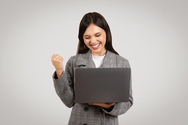 Joven empresaria alegre con laptop celebrando el éxito