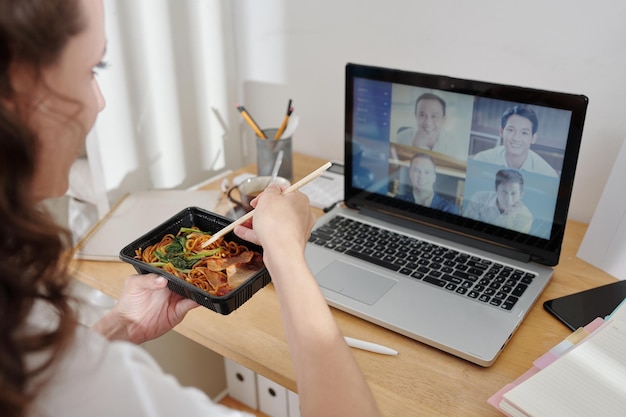 Joven empresaria almorzando en casa cuando tiene una lección en línea con colegas