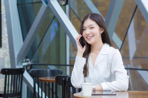 Joven empresaria asiática con cabello largo mientras trabaja fuera de la oficina está utilizando un teléfono inteligente